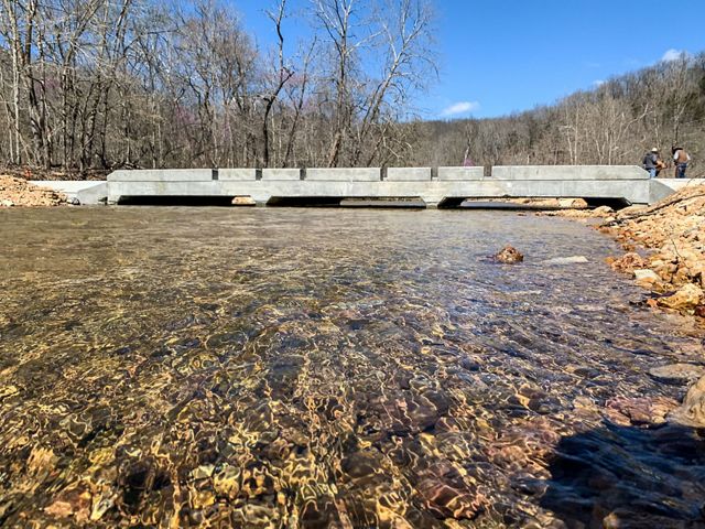 A bridge with large openings along the bottom crossing a small stream.