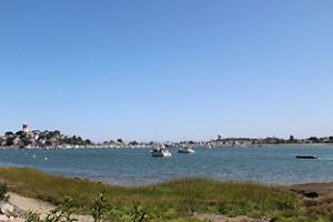 Looking south from the coast of Winthrop at the harbor and ocean beyond; houses on a peninsula are on the distance on the left; sky is bright blue.