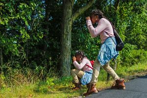 Two young people looking through binoculars into a wooded area.