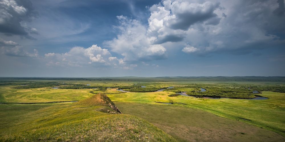 Landscape view from a high vantage point looking across a vast green plain with a long river winding through it.