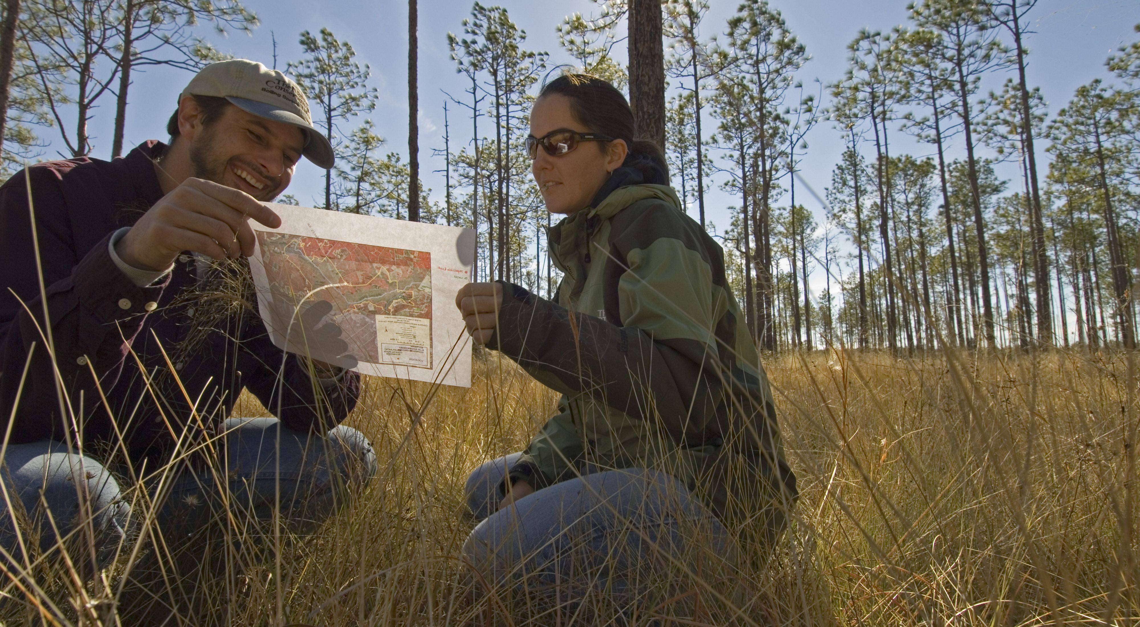 A man and woman crouch to study a map in a North Carolina forest.