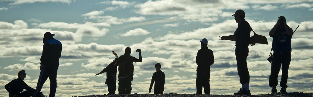 Silhouettes of people standing against a backdrop of sky with broken clouds.