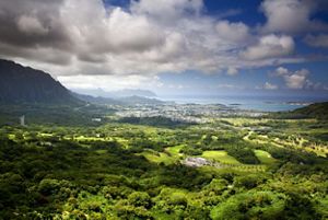 Landscape view overlooking a wide green valley on Oahu, Hawaii, with housing and the ocean in the distance.