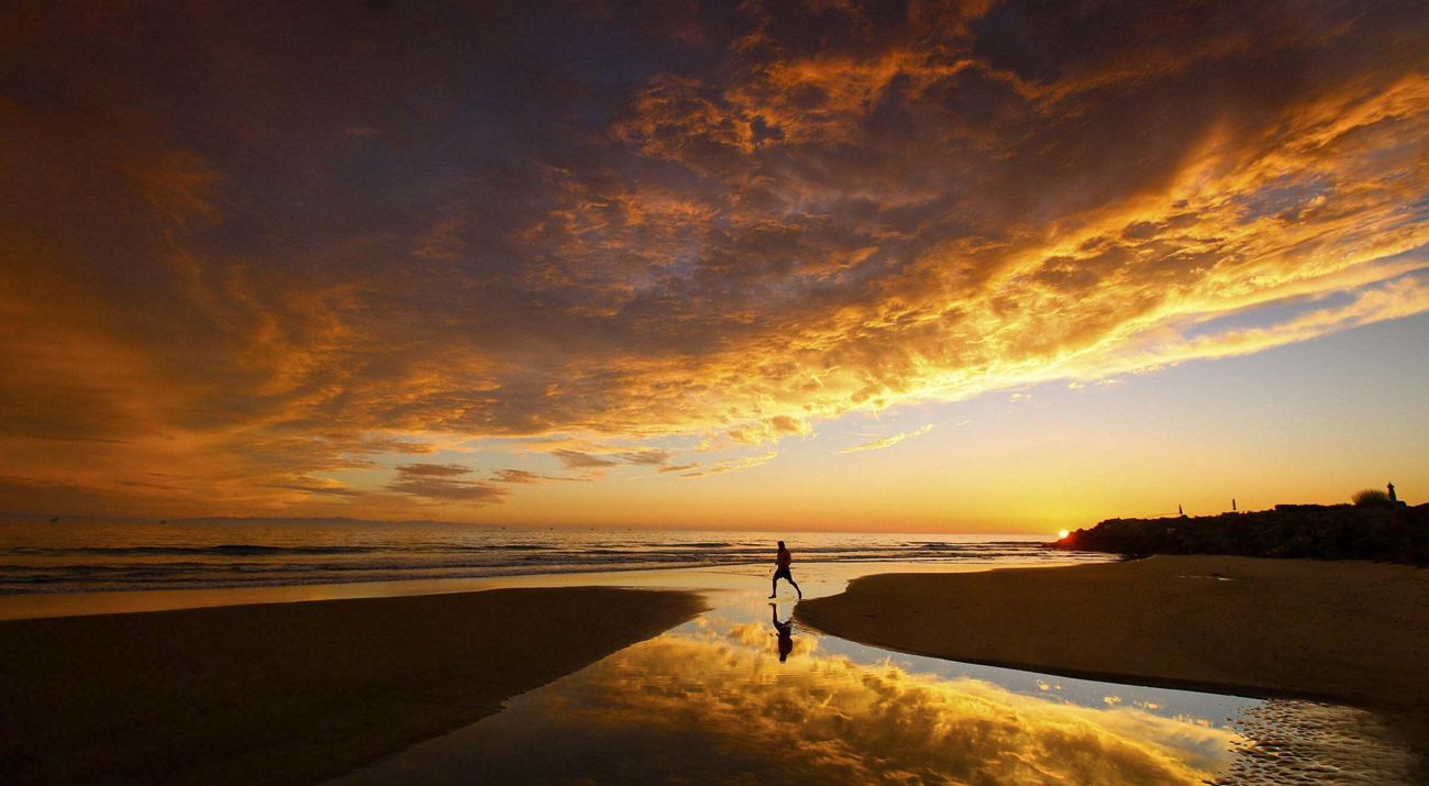 A person runs across a rivulet leading to the ocean at sunset.