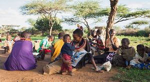 A seated woman dressed in colorful garb embraces a little boy.