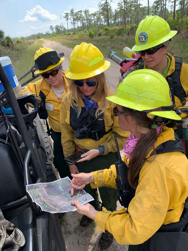 Photo of four women in fire gear looking at a map for a controlled burn. 