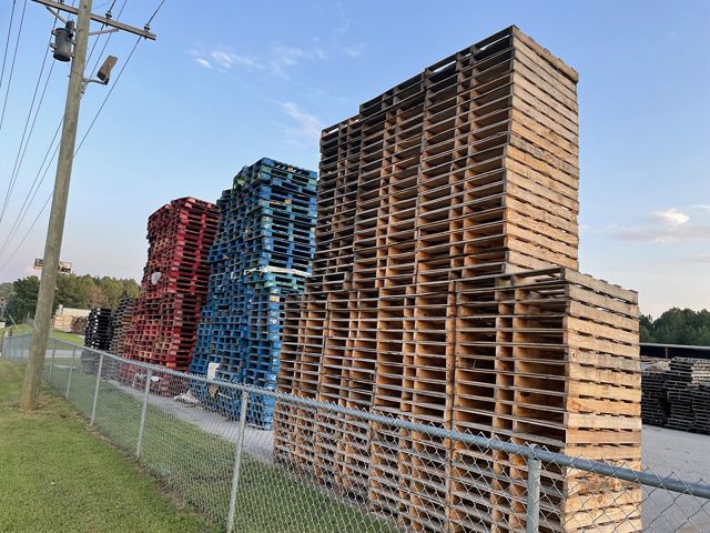 A stack of wooden pallets behind a chain link fence.