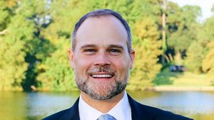 A man wearing a dark suit smiles at the camera.