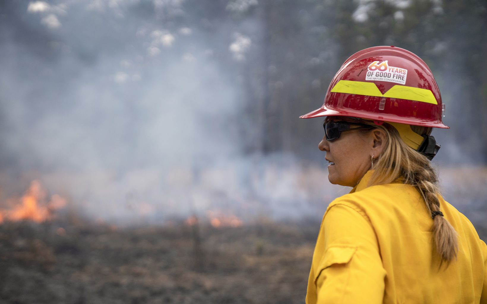 A woman in a hard hat surveying the site of a prescribed burn.