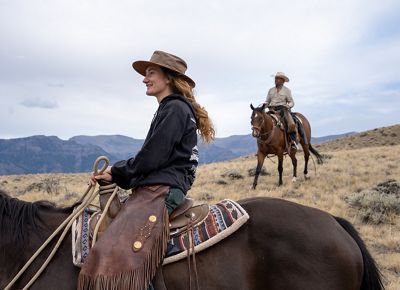 Two people on horseback with blue mountains behind them.