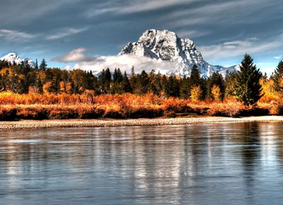 A snow capped mountain is reflected in the surface of the water on Jackson Lake.