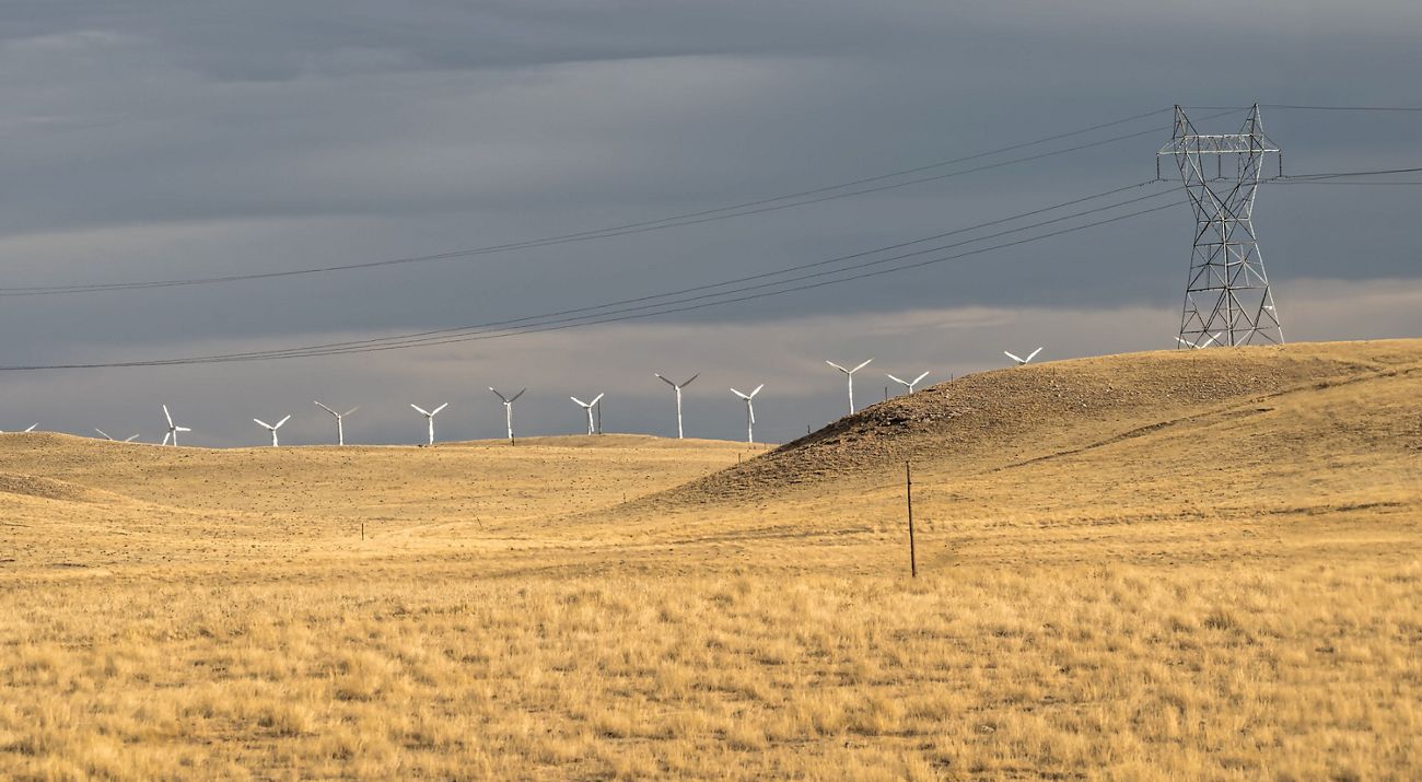 Field of grass with a powerline and wind turbines in the background.