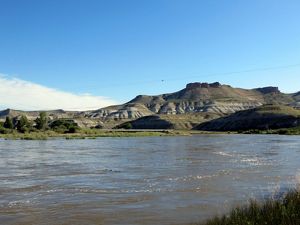 View looking across a wide, flat river toward hills in the distance.
