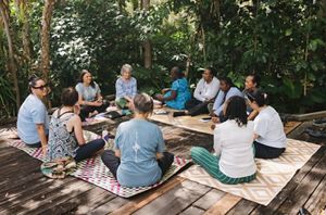 A group of women sit outdoors in a circle on mats.