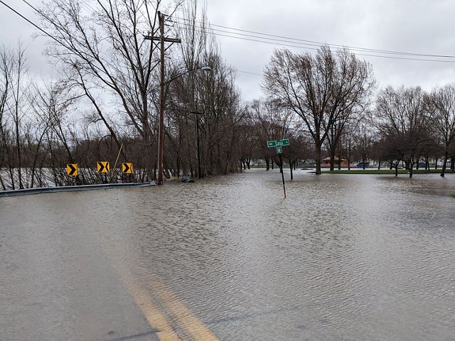 Flood waters cover a city roadway surrounding a post with green street signs.