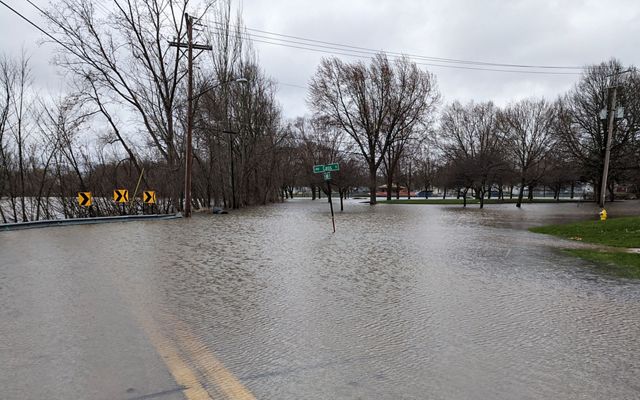 Flood waters cover a city roadway surrounding a post with green street signs.