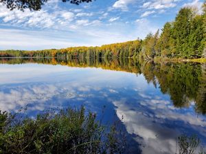 Glassy lake waters reflect the fall colors of trees along the shoreline.