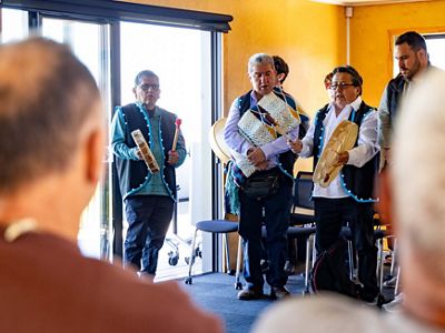 A band plays instruments gathered around a person sings in the center.