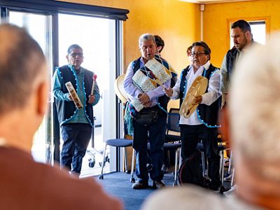 A small group of people with instruments stand and sing for an audience.