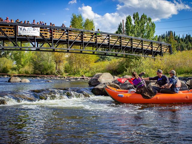 A group of people kayaking through a rushing river under a bridge.