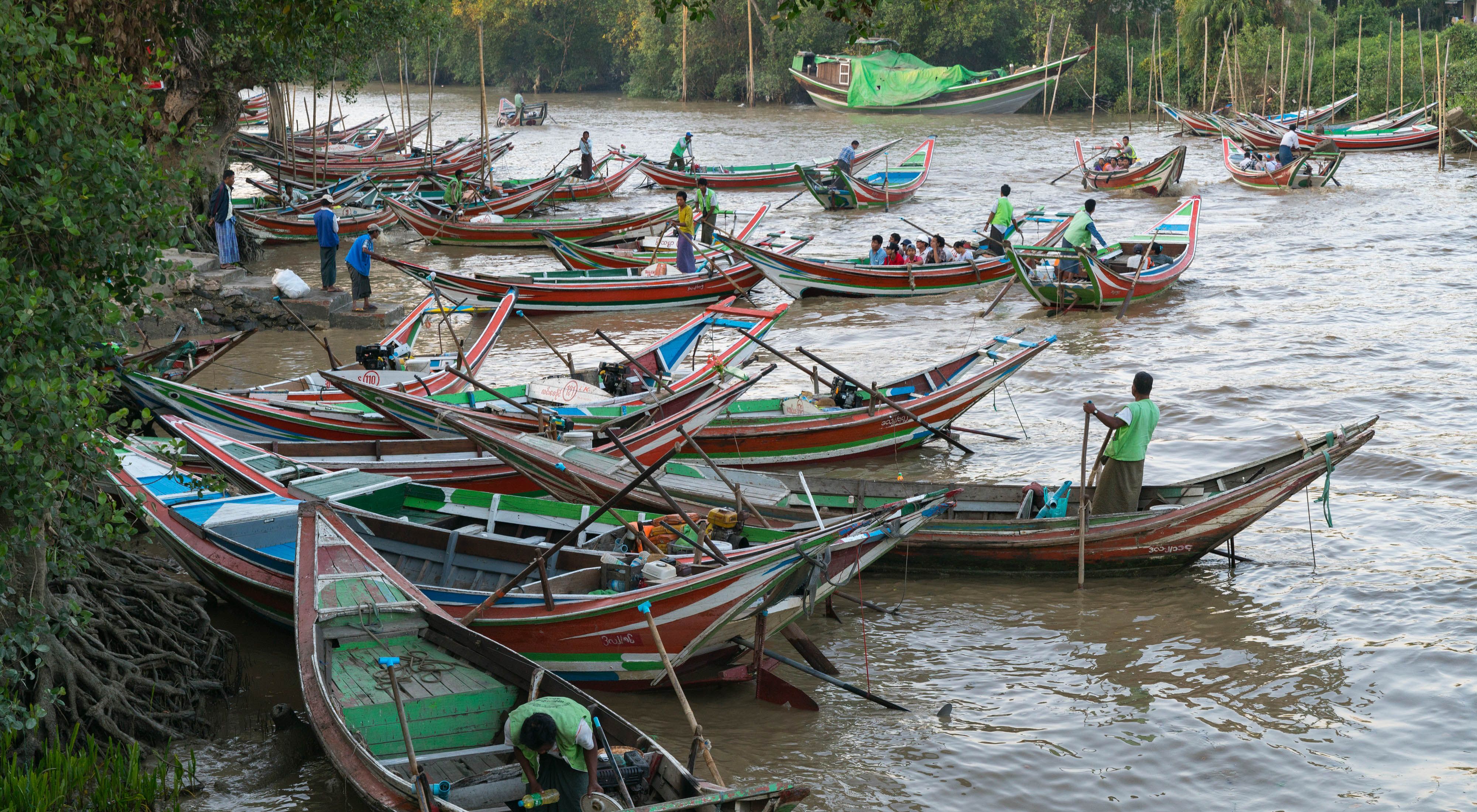 Dozens of brightly colored wooden fishing boats, some with fishermen in them, float in the Yangon River in Myanmar.