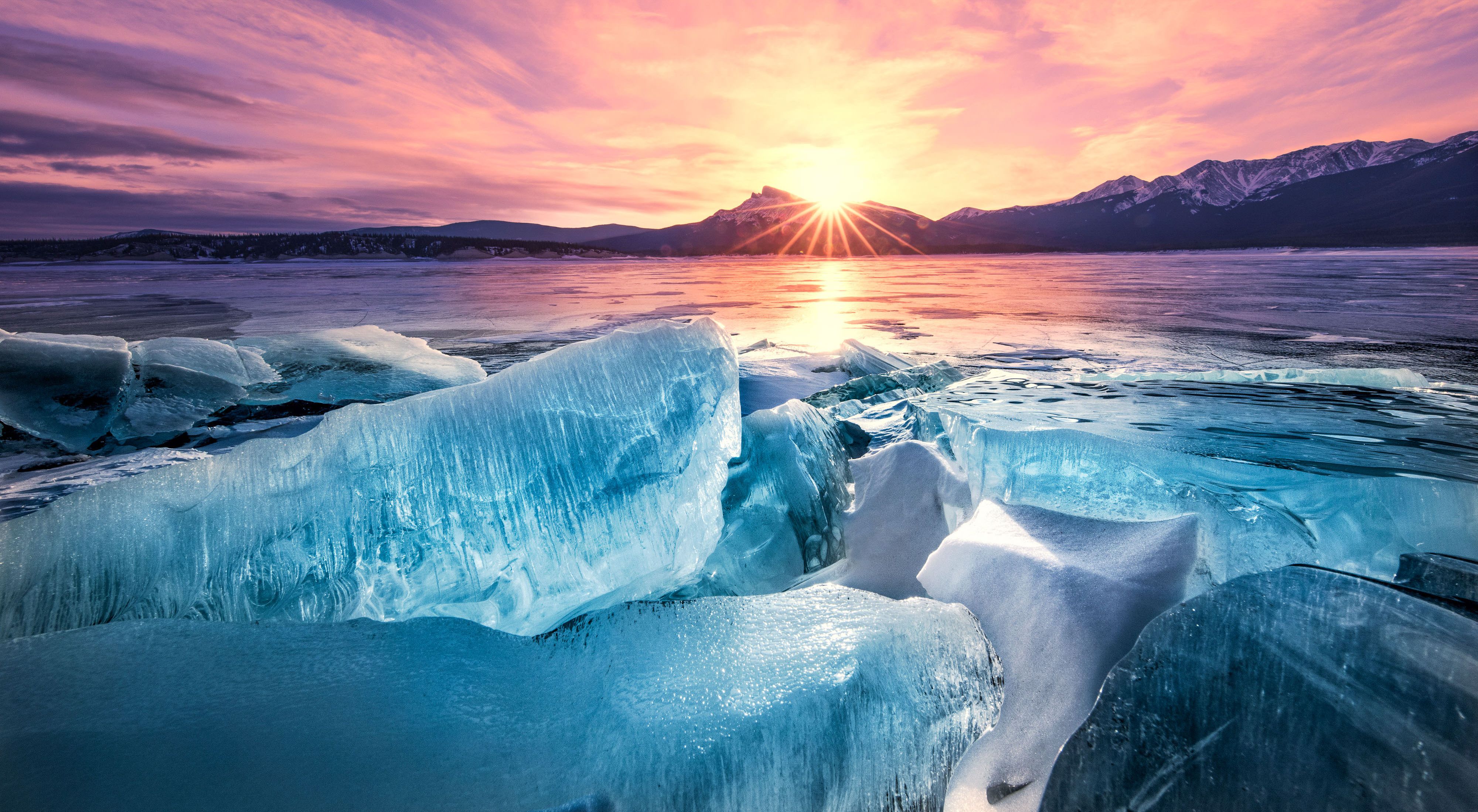 Massive ice blocks on a body of water with sun rising over mountains in the background.