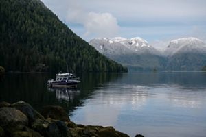 A boat on still water surrounded by forests and mountains.