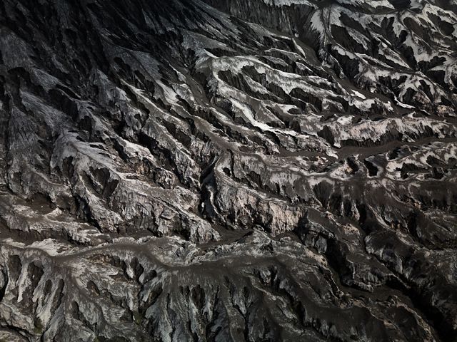 Mustard yellow fields frame a large fallow field. Hummocks of gray dirt are pushed up at the end of parallel tracks.