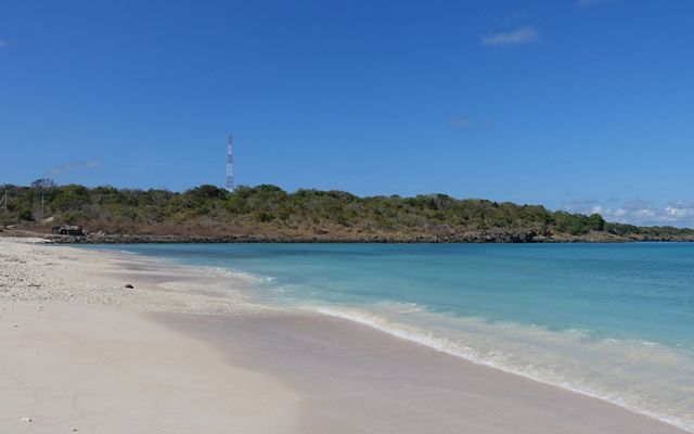 Blue ocean waters meet with white sand under a brilliant blue sky.