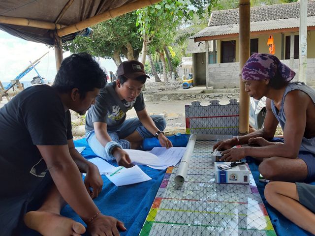 Three people sit around a measuring board while one of them explains something to the others.