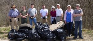 A group of smiling volunteers stand with the trash they've removed during a cleanup day.