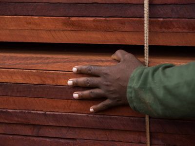 A hand on top of a stack of processed wooden planks.
