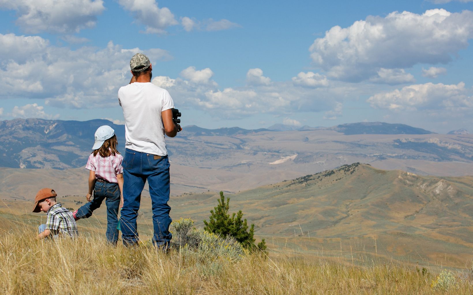 Adult and two children stand atop a hill looking across a sagebrush field.