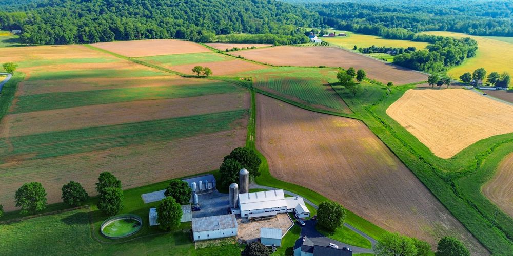 An aerial view of a farm house in between green and brown fields.