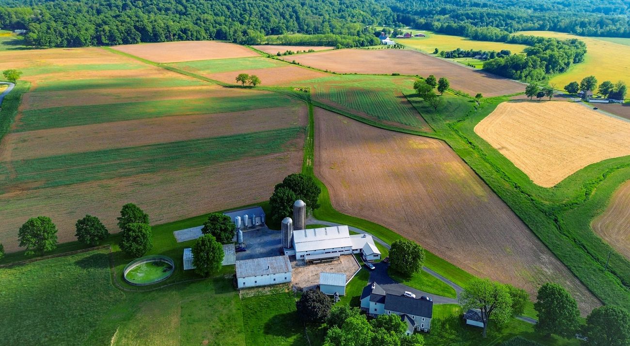 A view down of a farm house surrounded by green and brown fields.