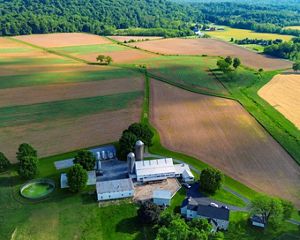 A view down of a farm house surrounded by green and brown fields.