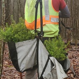 a person in reflective gear holding a bag of spruce bows.